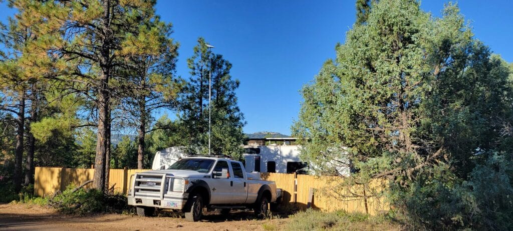 Image shows a white truck and a white fifth wheel RV with a Starlink RV satellite internet dish mounted on a 20-foot pole. 