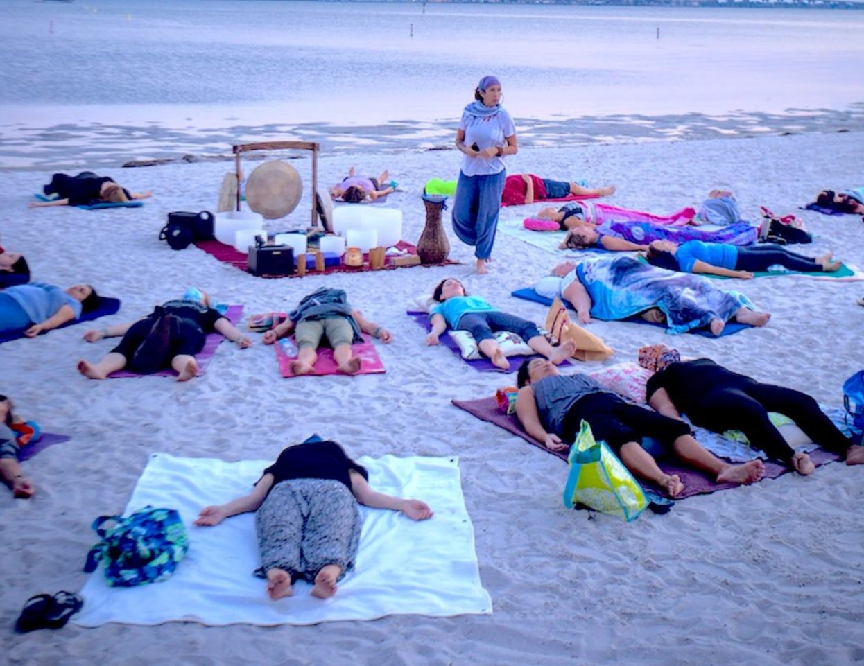 People lying on blankets on a beach during a sound bath session