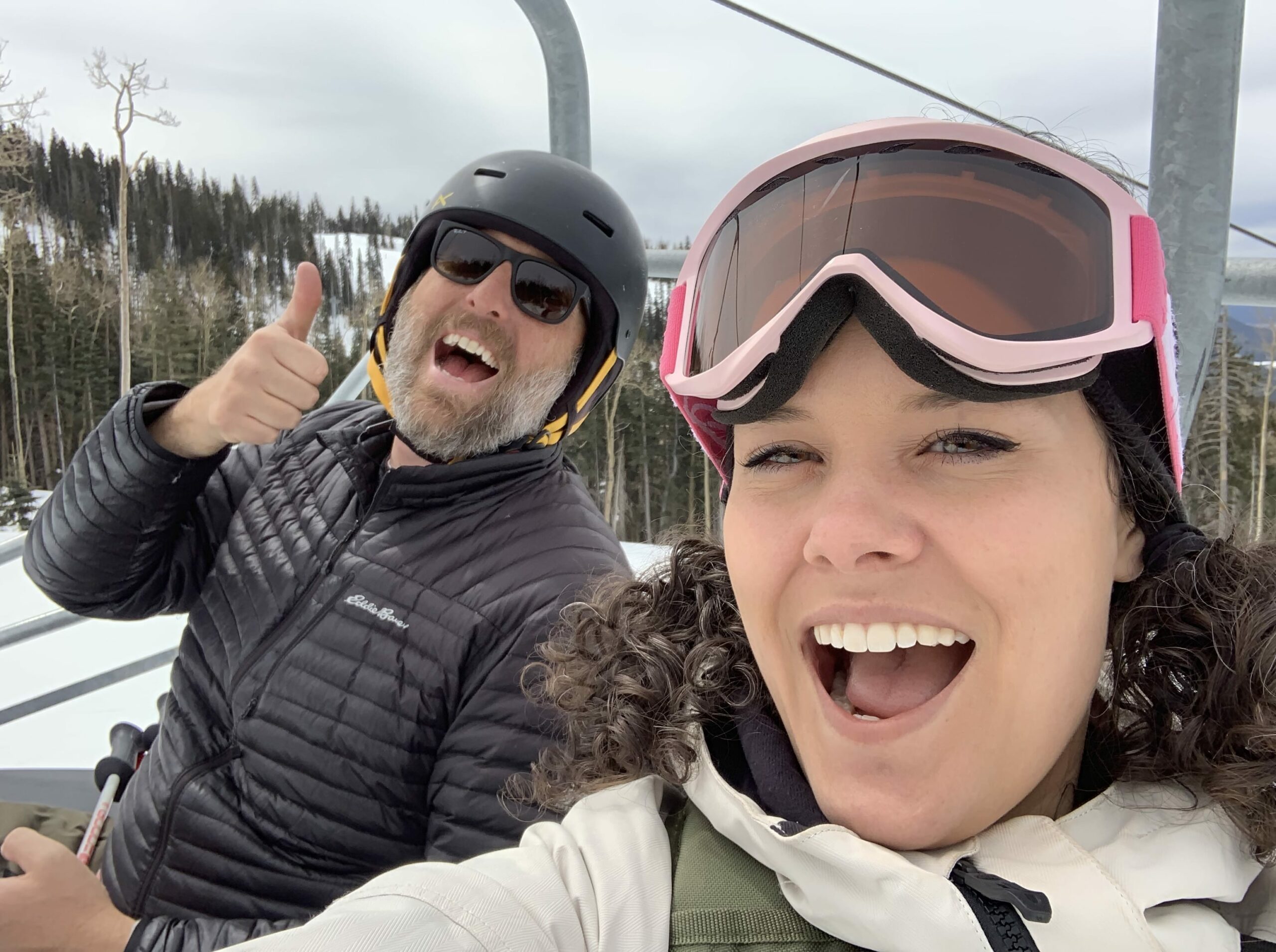 man and woman on ski lift waving at camera